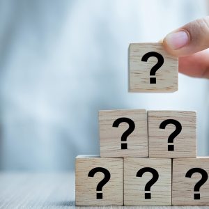 Businesswoman hand placing or pulling Questions Mark ( ? ) word with wooden cube block on the building. FAQ( frequency asked questions), Answer, Q&A, Information and Brainstorming Concepts